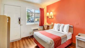 Habitación de hotel con cama, escritorio, silla, ventana con vistas y puerta.