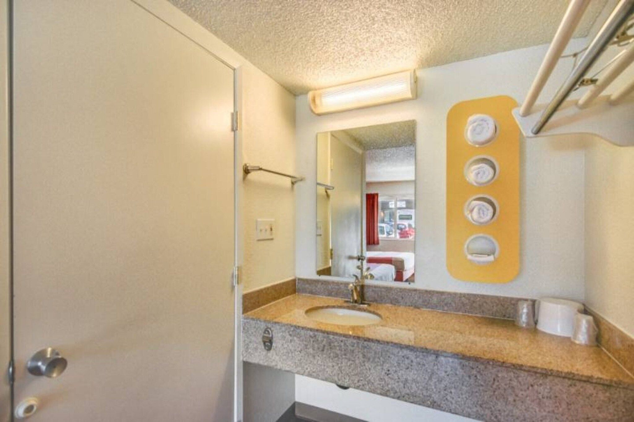 A bathroom with a sink, mirror, towel rack, and a wall-mounted soap dispenser.