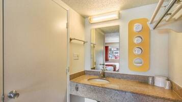 A bathroom with a sink, mirror, towel rack, and a wall-mounted soap dispenser.