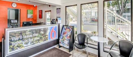 A hotel reception area with a counter, a clock, a magazine rack, and two chairs.
