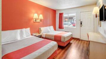 A hotel room with two beds, a desk, a TV, and a window with a view of the street.