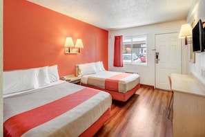 A hotel room with two beds, a desk, a TV, and a window with a view of the street. - 2 Full Beds | Non-Smoking (Stockton)