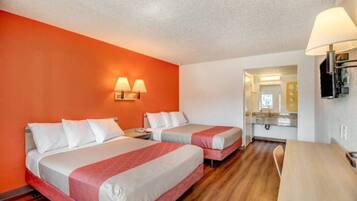 A hotel room with two beds, a desk, a chair, a mirror, and a lamp.