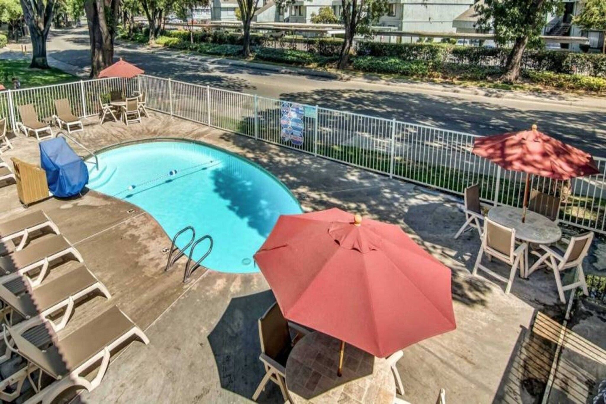 A swimming pool with lounge chairs and umbrellas, surrounded by a fence.