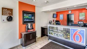 A reception area with a digital screen, a coffee station, and a counter with a sign.