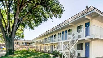 A motel with a two-story structure, a central staircase, and a large tree in the foreground.