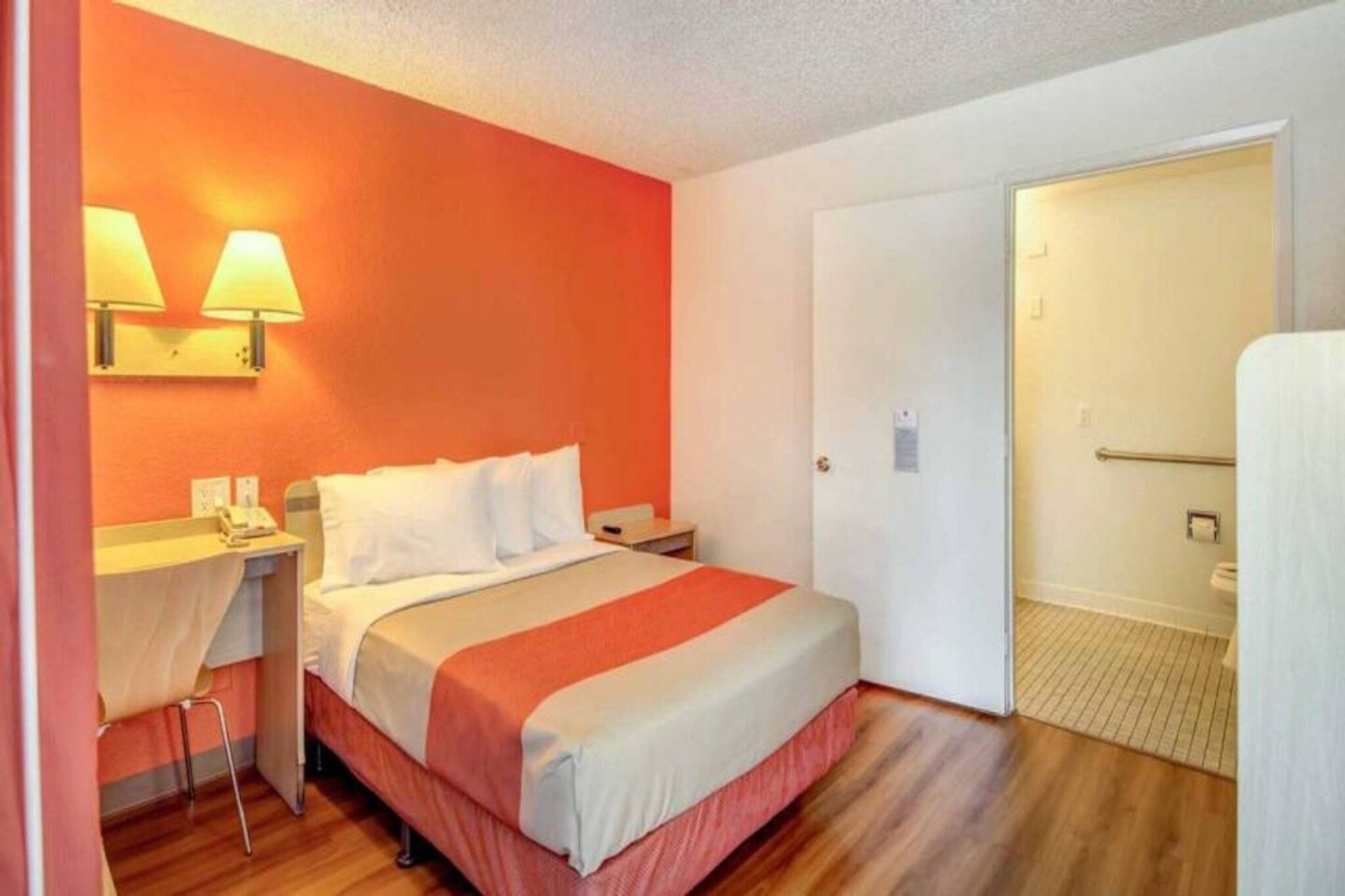 Una habitación de hotel con una cama, una mesita de noche, una lámpara, una silla y una puerta que da al baño.