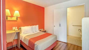 Una habitación de hotel con una cama, una mesita de noche, una lámpara, una silla y una puerta que da al baño.