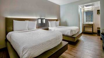 A hotel room with two beds, a wooden floor, and a view of the outside.