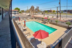 A swimming pool with lounge chairs and umbrellas, surrounded by a fence, with buildings in the background. - 2 Queen Beds | Kingman (Kingman)