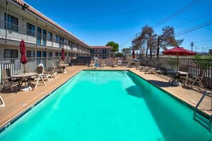 Una piscina con sillas de descanso y sombrillas, rodeada por un edificio con varios balcones.