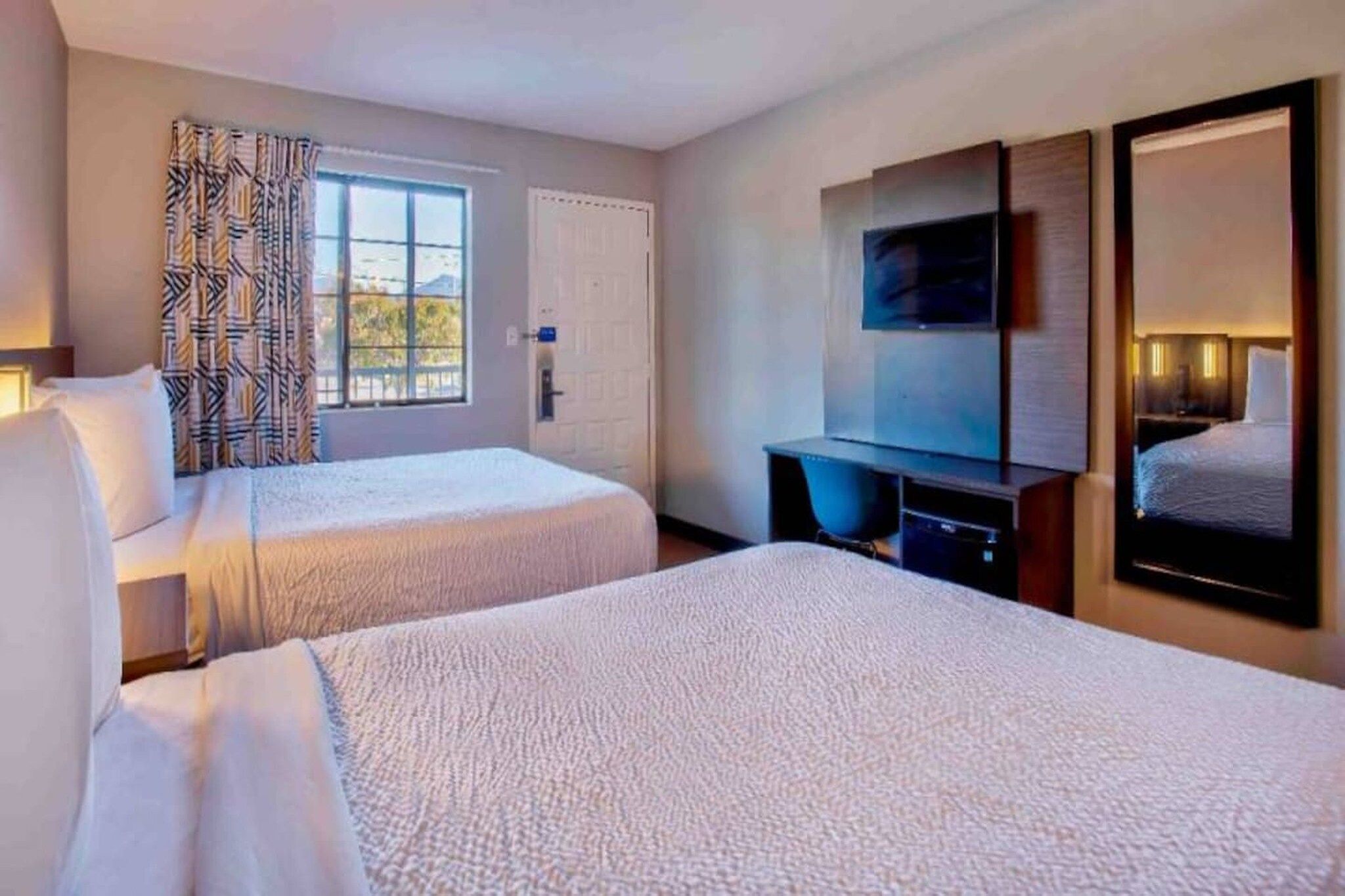 A hotel room with two beds, a television, a desk, and a window with curtains.