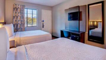 A hotel room with two beds, a television, a desk, and a window with curtains.