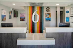 A reception area with two counters, a large number '6' on the wall, and various informational posters. - 2 Queen Beds | Kingman (Kingman)