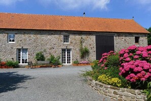 A stone building with a red-tiled roof, a gravel driveway, and a garden with pink flowers. - Holiday home in Vesly with swimming pool (Vesly)