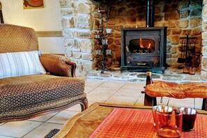 A cozy room with a stone fireplace, a patterned armchair, and a bench. - Holiday home in Vesly with swimming pool (Vesly)