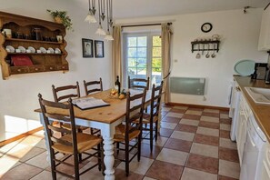 A dining area with a wooden table and chairs, a kitchen with appliances, and a window with curtains. - Holiday home in Vesly with swimming pool (Vesly)