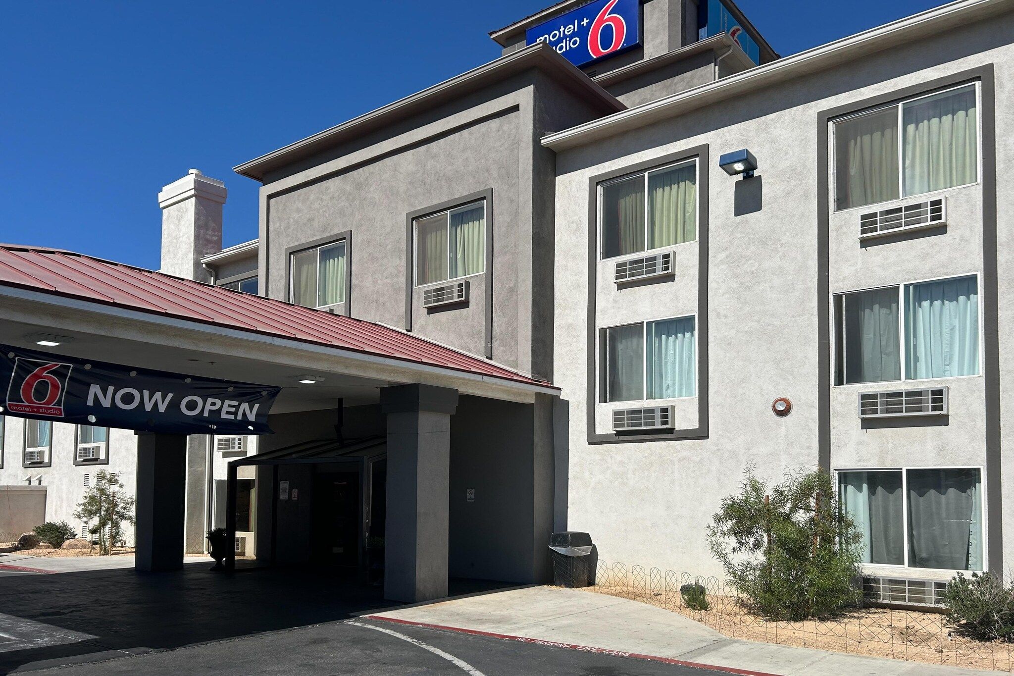 A motel with a 'NOW OPEN' sign, a covered entrance, and a clear blue sky.