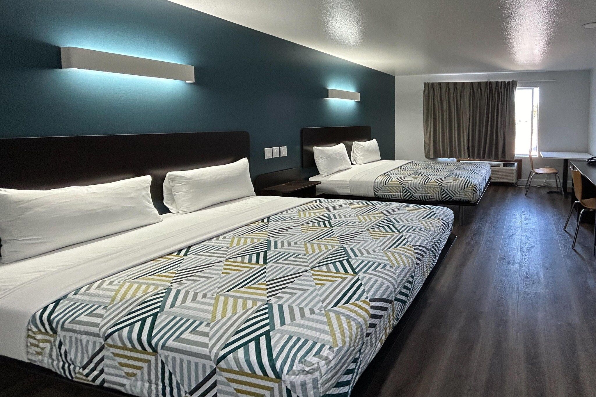 A hotel room with two beds, a desk, and a chair.