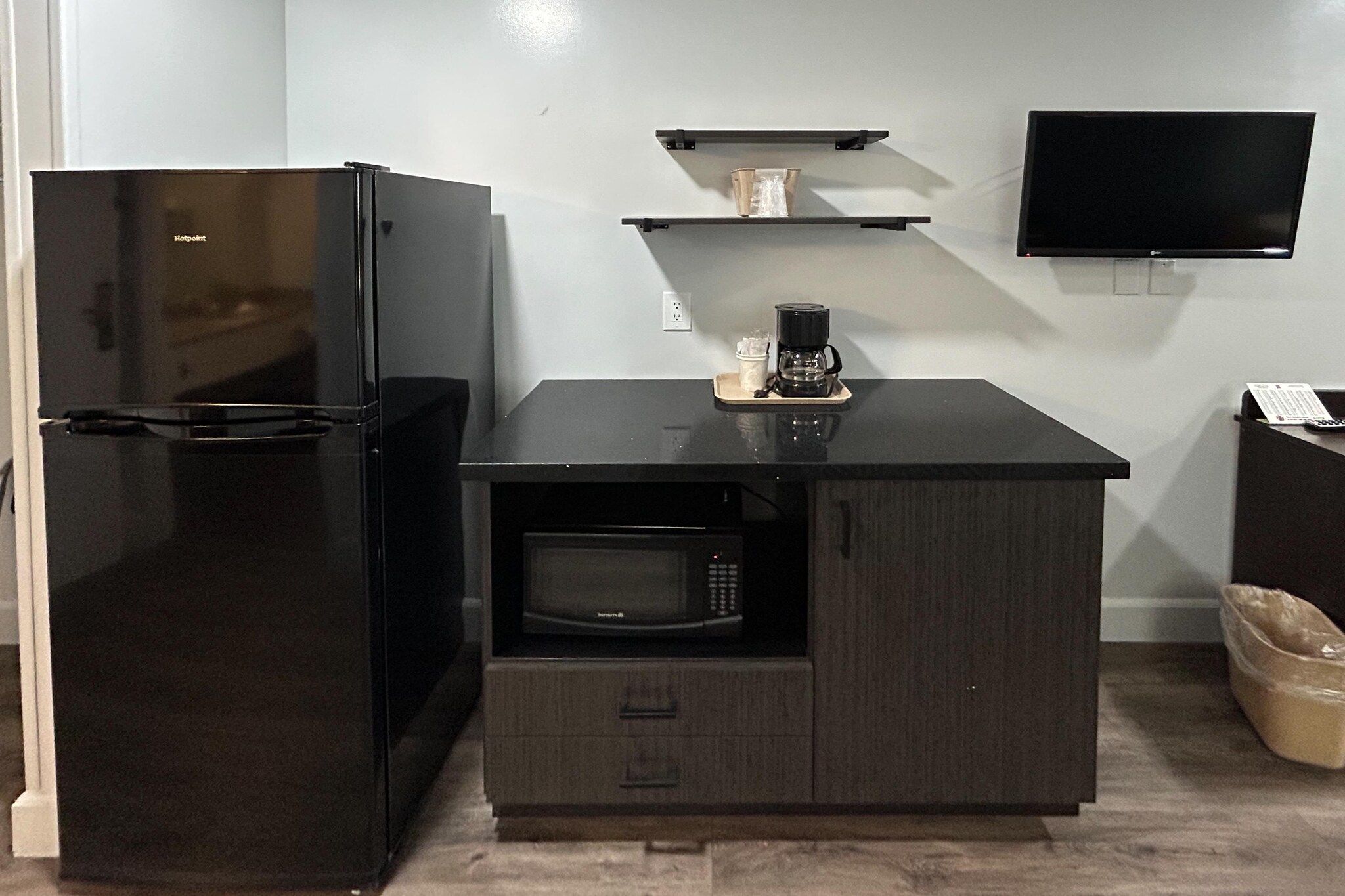 A compact kitchenette with a black refrigerator, a microwave, and a coffee maker on a black countertop.