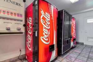 Tres máquinas expendedoras de Coca-Cola en una habitación con suelo de baldosas y una puerta blanca.