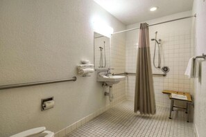 A standard hotel bathroom with a shower, toilet, sink, and a small table with a towel.