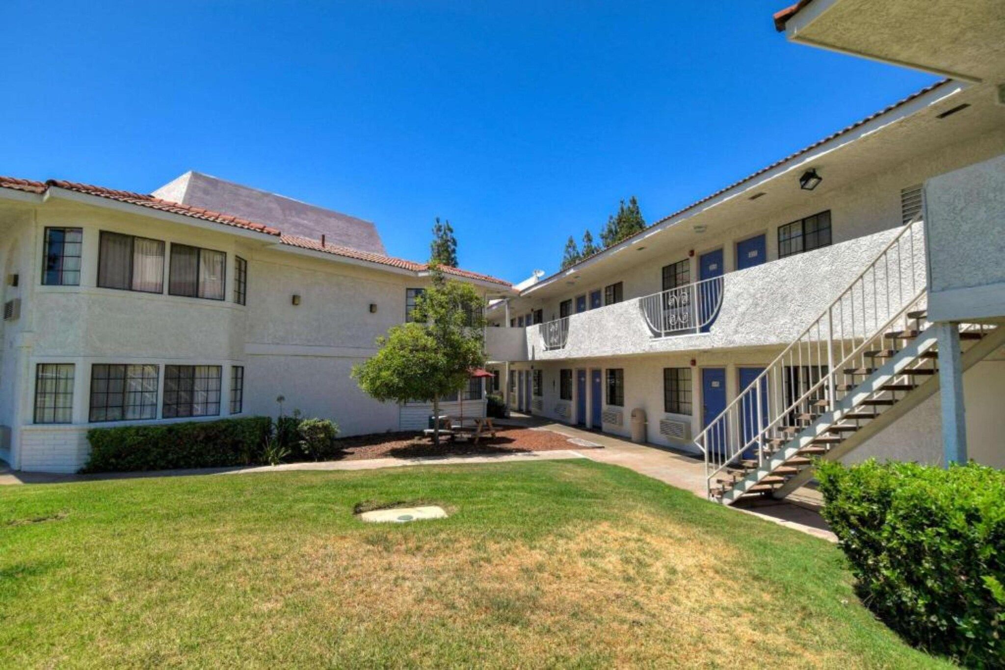A courtyard with two-story buildings, a tree, and a grassy area.