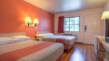 A hotel room with two beds, a desk, a chair, a window with curtains, and a door.