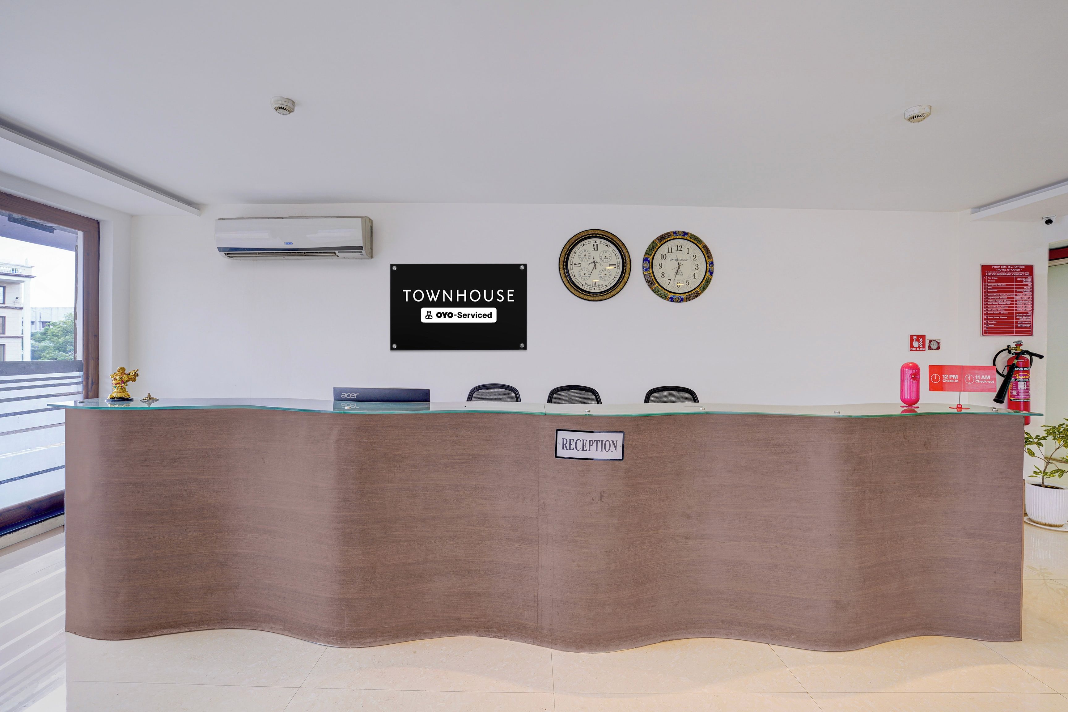 Un mostrador de recepción con un letrero que dice 'RECEPTION', dos relojes de pared y un letrero con 'TOWNHOUSE' que indica OYO-Service.