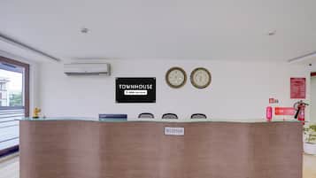 Un mostrador de recepción con un letrero que dice 'RECEPTION', dos relojes de pared y un letrero con 'TOWNHOUSE' que indica OYO-Service.