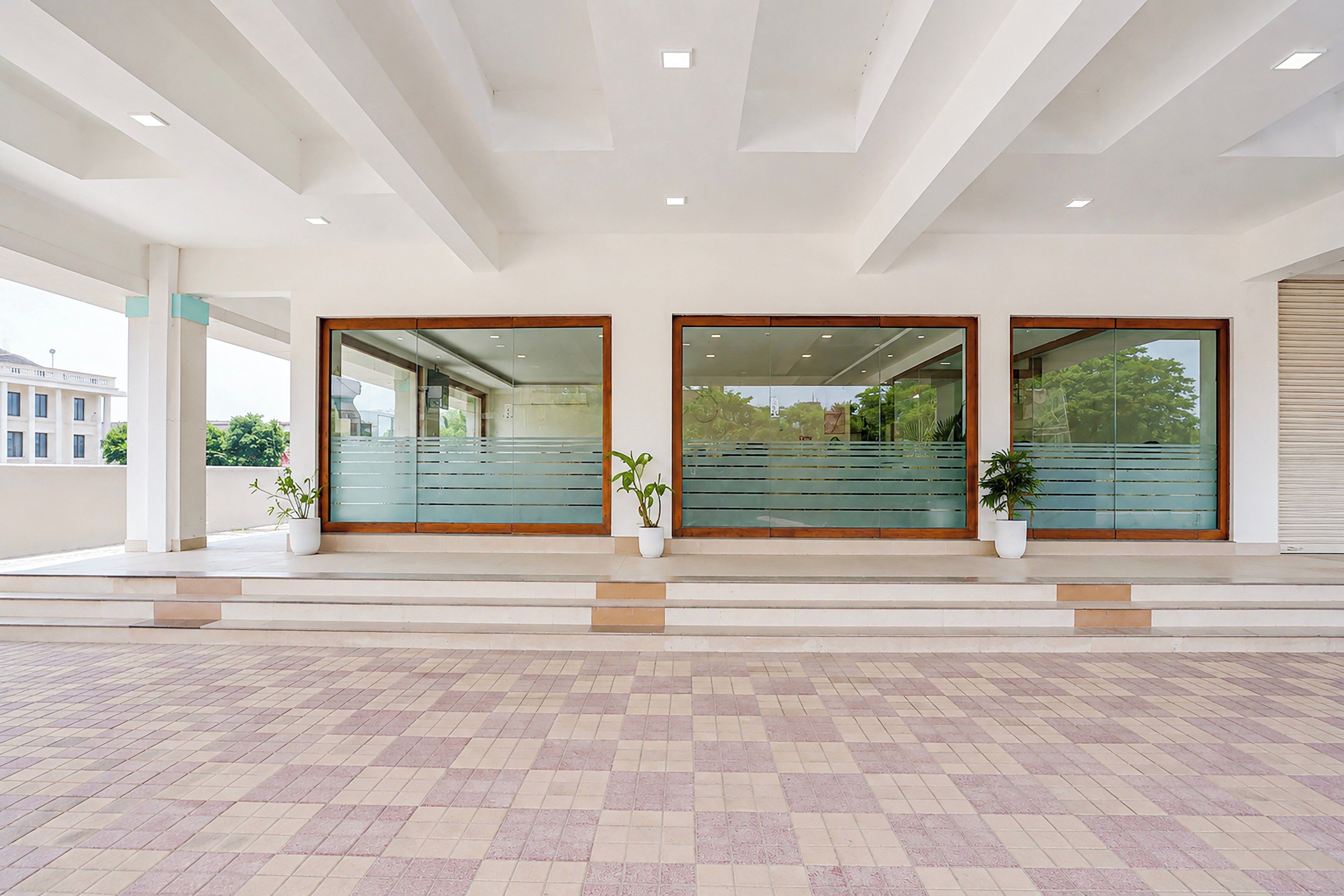 A modern building entrance with a tiled floor, large glass doors, and potted plants.