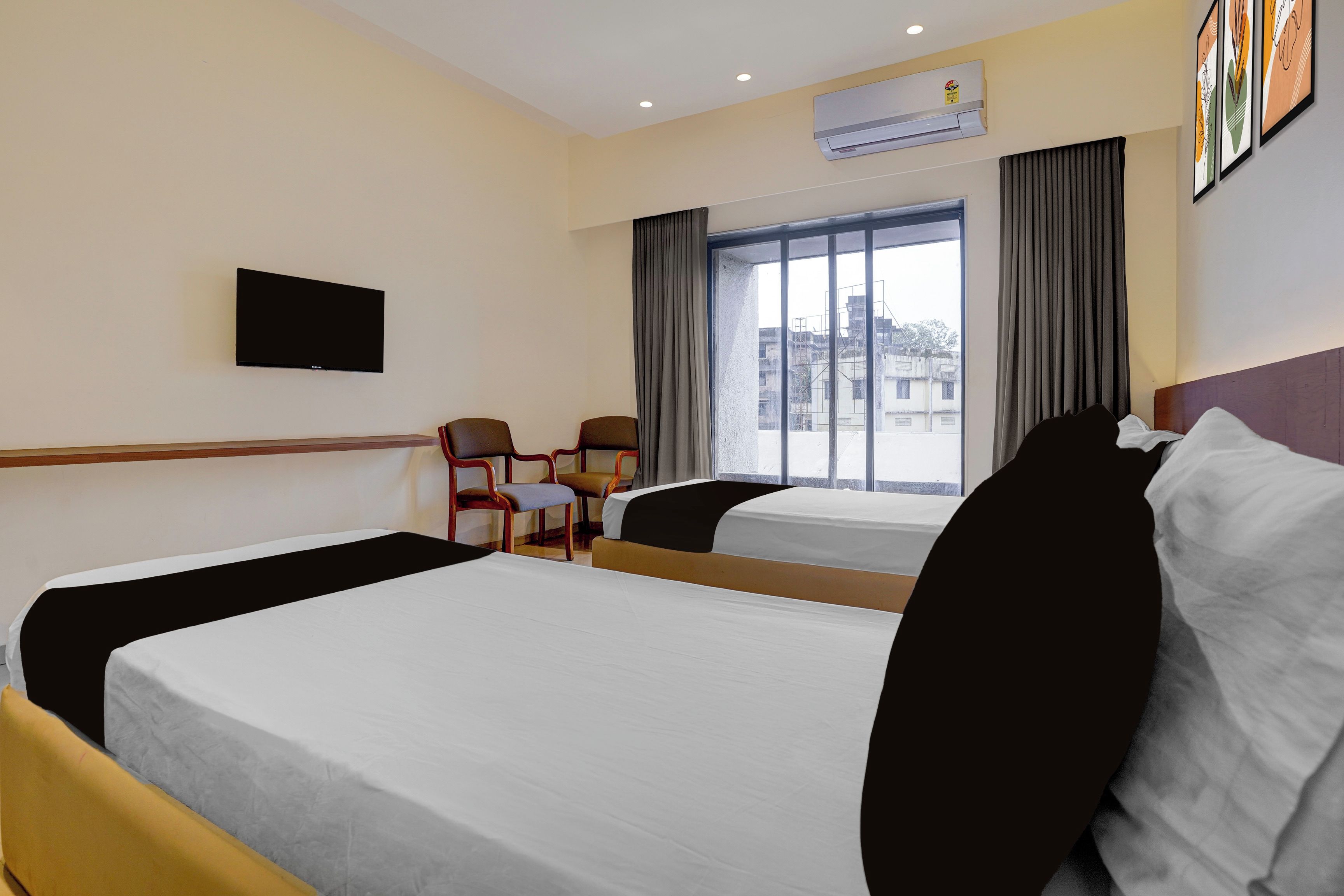 A hotel room with two beds, a flat-screen TV, a window with curtains, and an air conditioning unit.