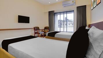 A hotel room with two beds, a flat-screen TV, a window with curtains, and an air conditioning unit.