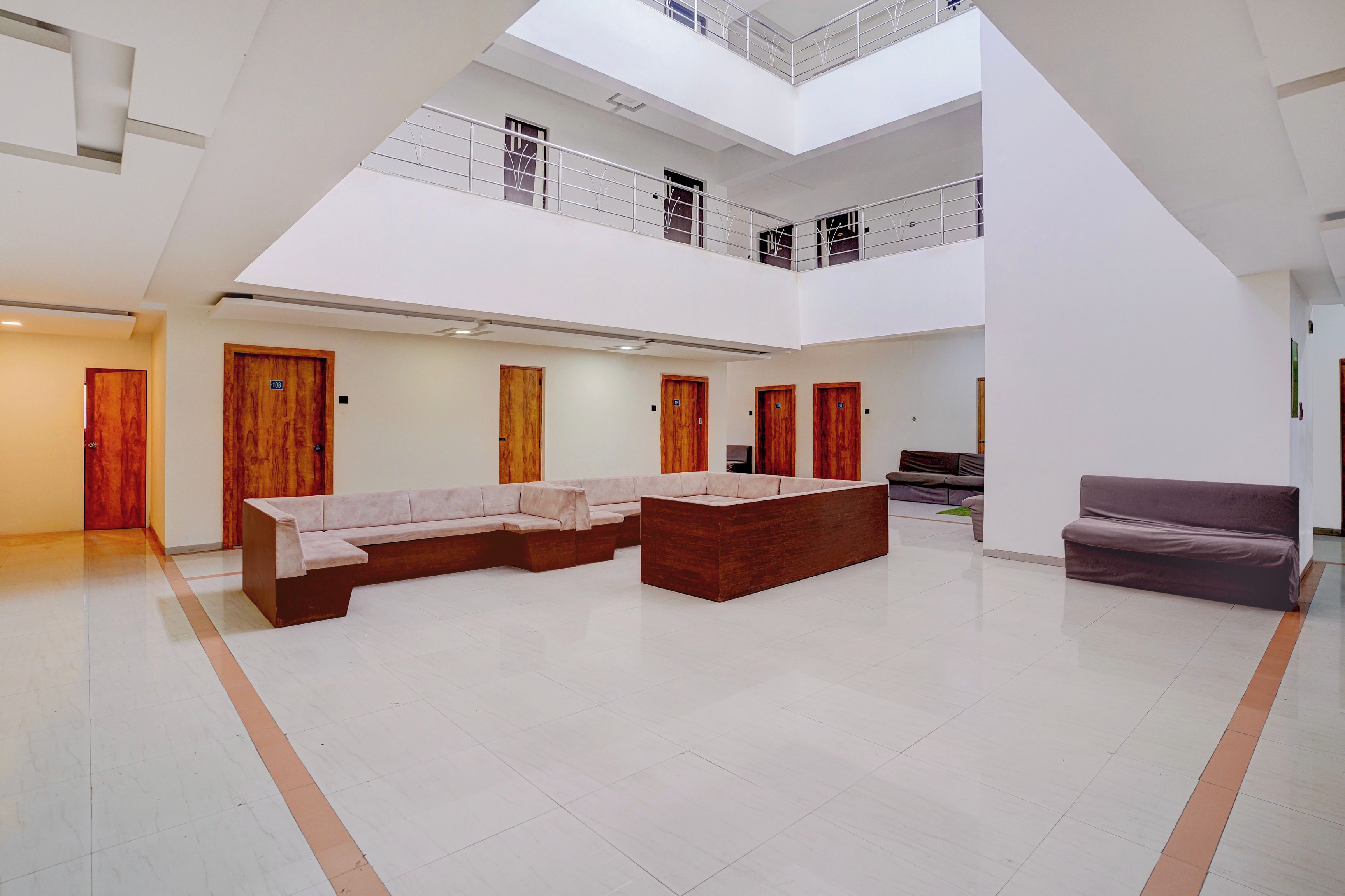 A spacious atrium with a high ceiling, a central seating area with a sofa and a bench, and a staircase leading to an upper level.