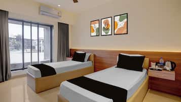 A hotel room with two beds, a window with curtains, a wall-mounted air conditioner, and a nightstand with a water bottle and kettle.