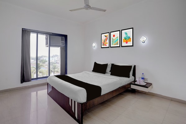 A bedroom with a bed, a nightstand, a water bottle, and a window with curtains. - Townhouse RTO Office Silvassa (Silvassa)