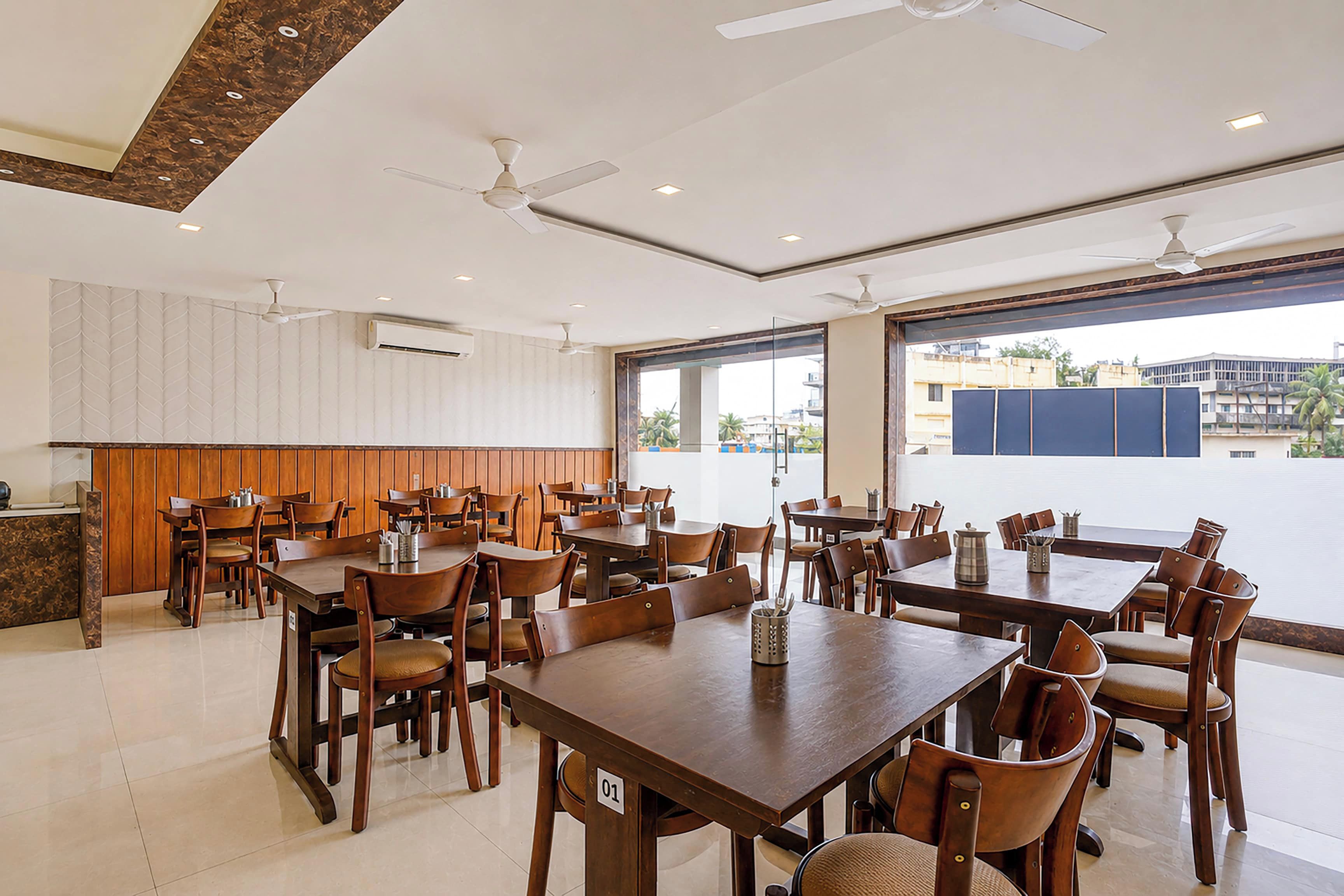 Un comedor amplio con varias mesas y sillas, ventiladores de techo y ventanas grandes que ofrecen vistas al exterior.