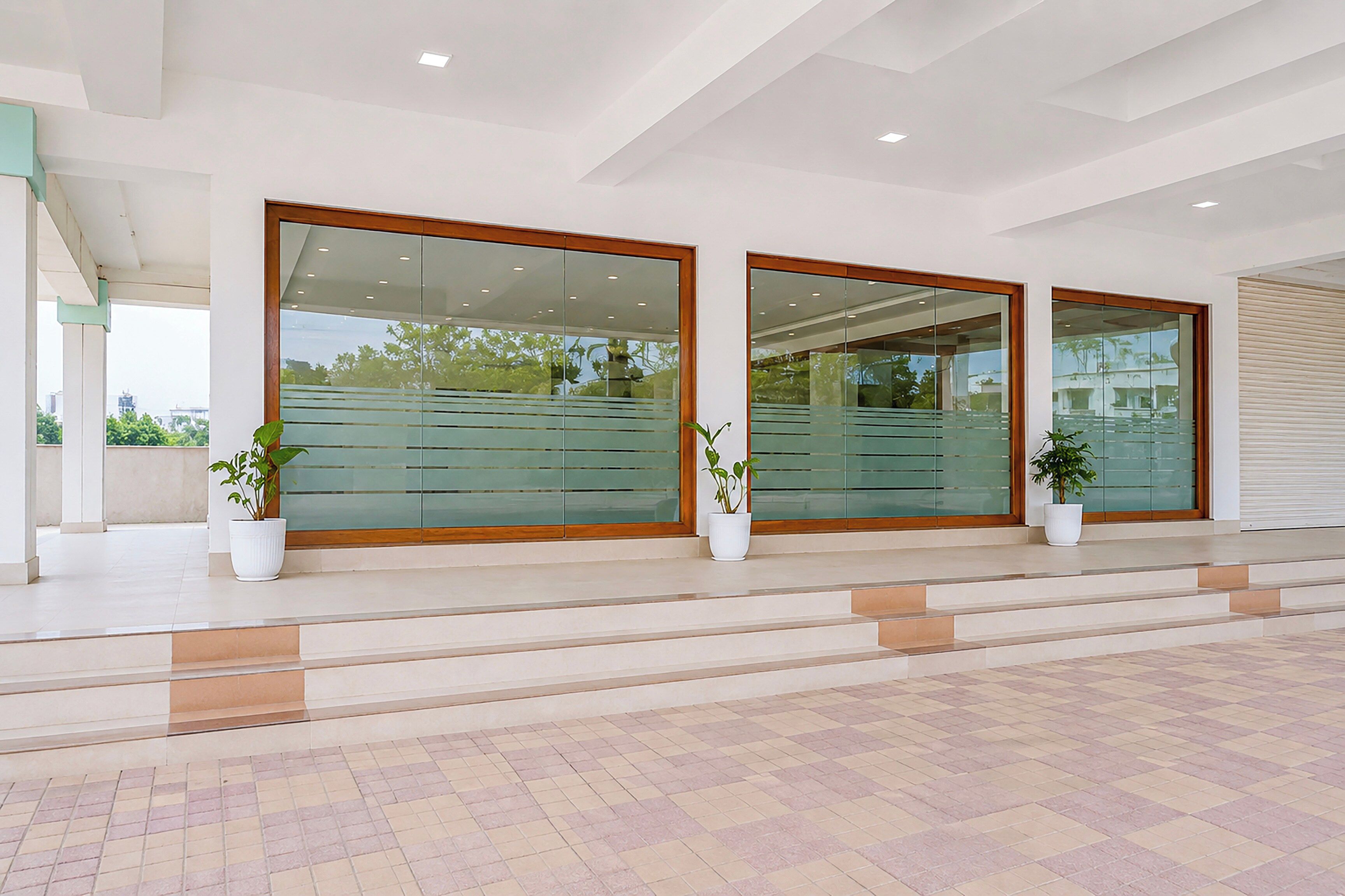 A modern building entrance with glass doors, potted plants, and a tiled floor.