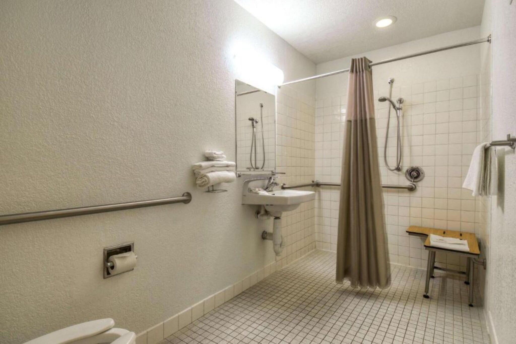 A standard hotel bathroom with a shower, toilet, sink, and a small table with a towel.