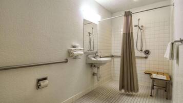 A standard hotel bathroom with a shower, toilet, sink, and a small table with a towel.