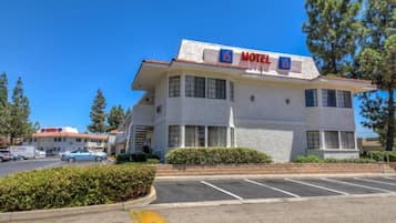 A motel with a red sign, a parking lot, and a clear blue sky.