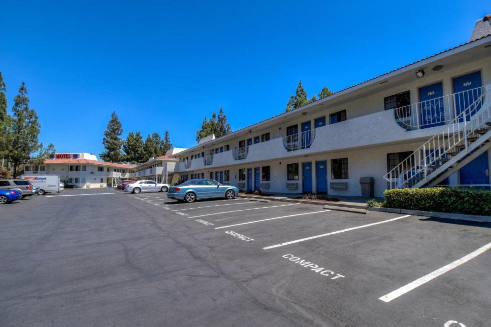 A motel with a parking lot, compact parking spaces, and a building with multiple rooms.