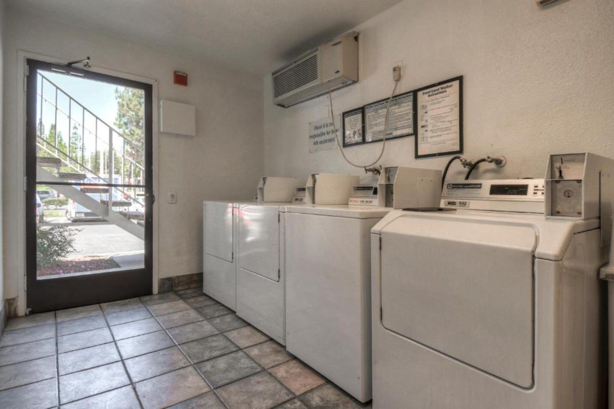 Une buanderie avec une porte donnant sur l’extérieur, un lave-linge, un sèche-linge et un climatiseur fixé au mur.