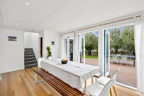 Ein moderner Essbereich mit einer Holzbank, einem weißen Tisch und Stühlen, der auf eine Terrasse mit Außenbestuhlung hinausführt.