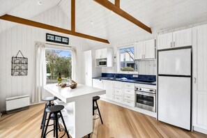 A modern kitchen with white cabinetry, a central island, and a view to the outdoors. - Aireys Sea & River Retreat family friendly escape (Aireys Inlet)