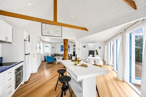 A modern kitchen with a central island, bar stools, and a dining area with a table and chairs. - Aireys Sea & River Retreat family friendly escape (Aireys Inlet)