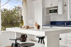 Una cocina moderna con una isla central, armarios blancos, un microondas y vistas a árboles.