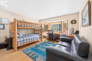 Ein Zimmer mit Etagenbetten, einem Schreibtisch, einer Ledersofa und einem farbenfrohen Teppich.