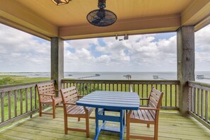 Een overdekt terras met een tafel en stoelen, met uitzicht op een waterlichaam met steigers.