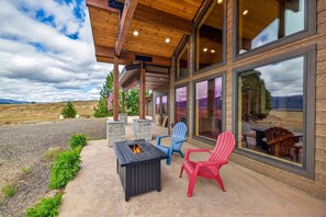 A covered patio with a fire pit, outdoor seating, and a view of the landscape. - The Cascade Ranch House | 24 Acres of Idaho Mountain Country (Cascade)
